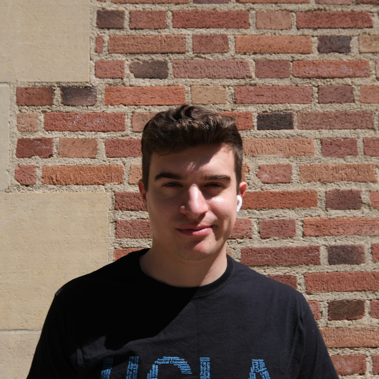 Young man wearing one AirPod and smirking while standing in front of a brick wall. His face is obscured by a shadow. 